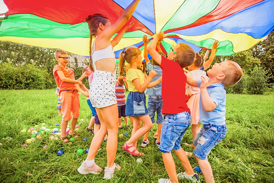 enfants sous une bache parachute colorée dans l'herbe qui jouent au flower cmaping la chenaie